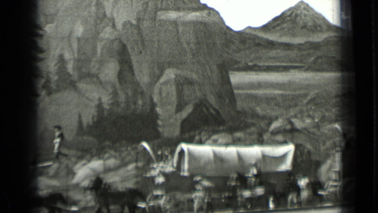 Covered wagon and draft animals pass before a painted rocky mountain backdrop.