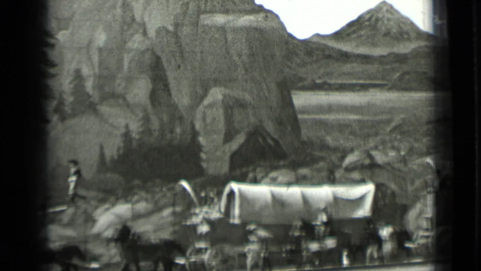 1937 San Francisco 8mm frame showing a covered wagon display with animals, small figures, rocks, pine trees, and a painted lake backdrop.