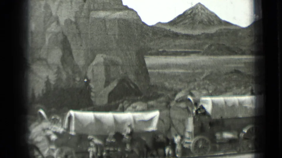 A home-movie frame records the covered wagon diorama from a visitor viewpoint, with animals, figures, rocks, and distant painted water.