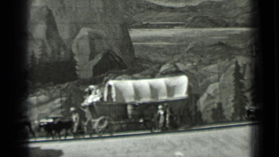 1937 San Francisco 8mm frame showing a covered wagon, oxen, and small pioneer figures in a scenic diorama.