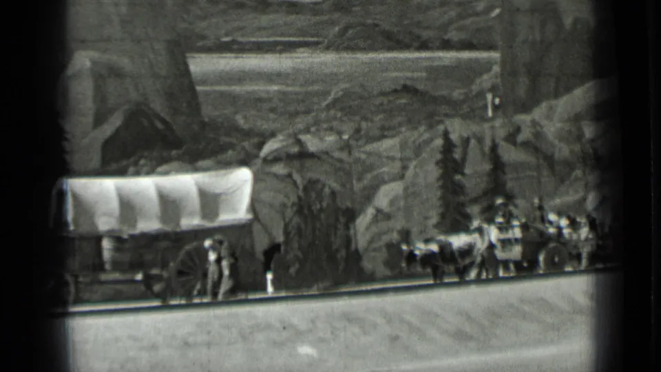 Black-and-white 1937 San Francisco frame of a pioneer wagon display with oxen, travelers, rocks, and painted hills.