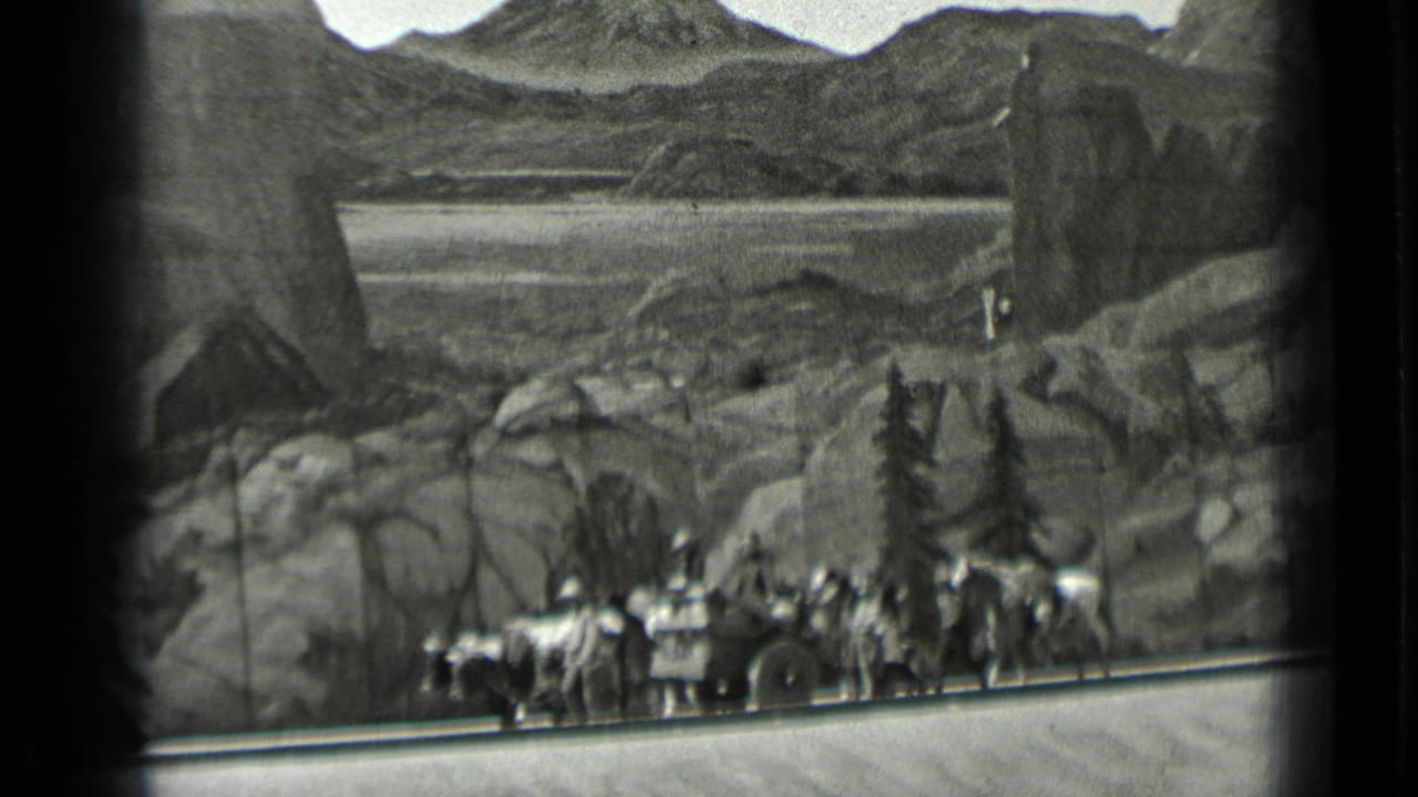 People and horses near a wagon in front of a painted mountain backdrop.