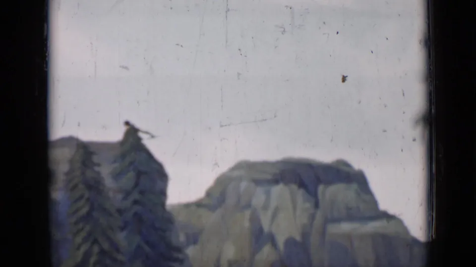 Final 8mm frame showing a pine tree, painted rocky mountain forms, pale sky, and the film edge.