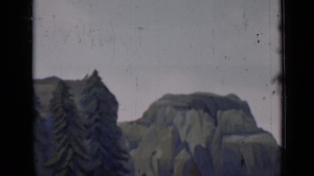 Painted mountain backdrop with dark trees at the left edge of an 8mm frame.