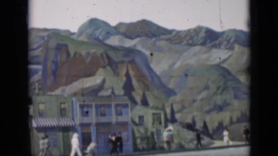 Soft 8mm frame from 1937 San Francisco showing distant pedestrians beside a painted street set and mountain backdrop.
