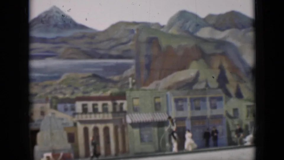 1937 San Francisco 8mm frame showing a staged streetscape with painted shops, mountain scenery, and people by high-wheel bicycles.