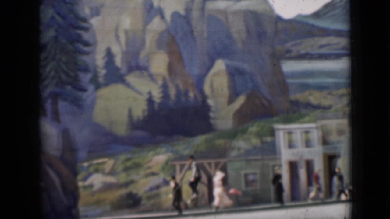 A late frame from the 1937 San Francisco clip shows people and high-wheel bicycles in front of trees, facades, and painted mountain scenery.
