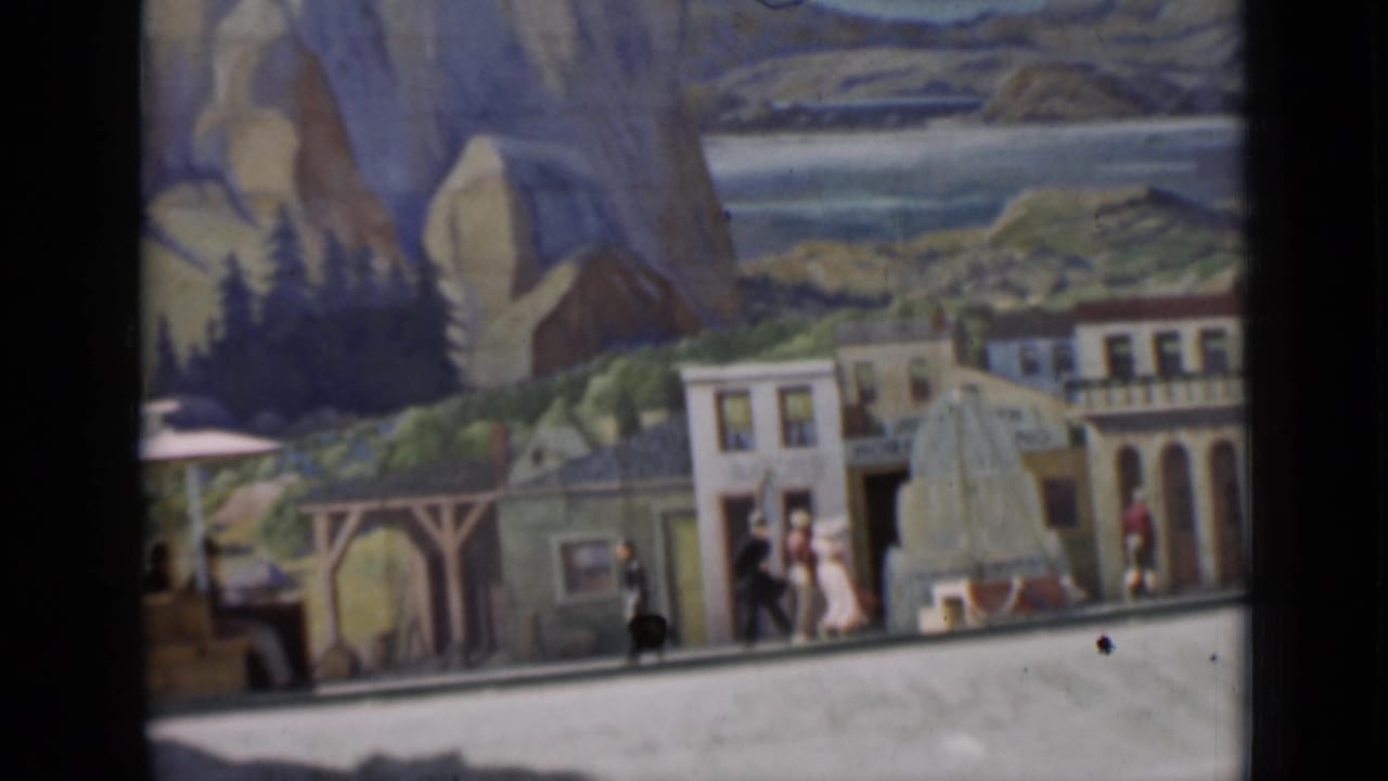 Miniature street scene in the 1937 home-movie footage, with small figures, building facades, and a painted mountain-and-lake backdrop.