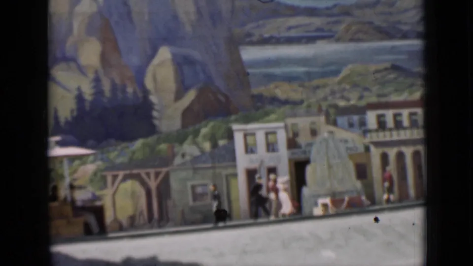 Miniature street scene in the 1937 home-movie footage, with small figures, building facades, and a painted mountain-and-lake backdrop.