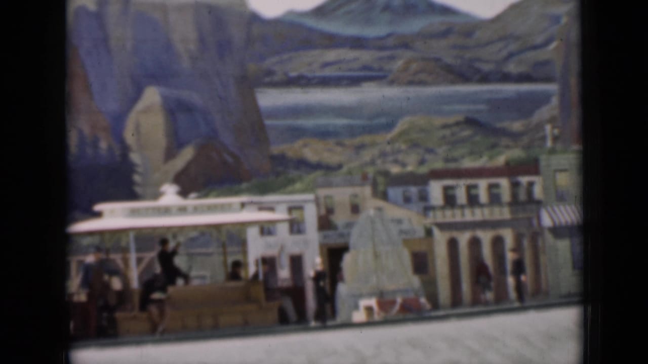 A 1937 8mm frame shows a model transit display with a station canopy, storefronts, small figures, and painted mountain scenery.