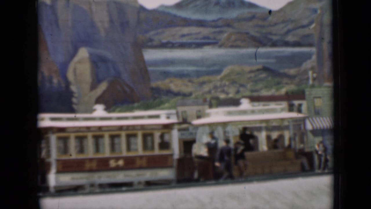 Red-and-cream trolley marked 54 moves through the miniature town scene in San Francisco-associated 1937 8mm footage.