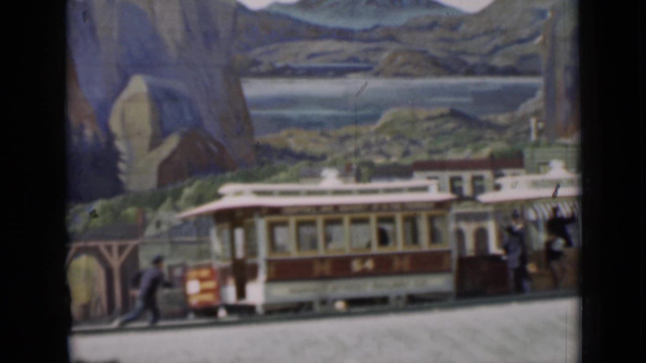 Miniature trolley passes storefronts in front of a painted mountain and water backdrop.