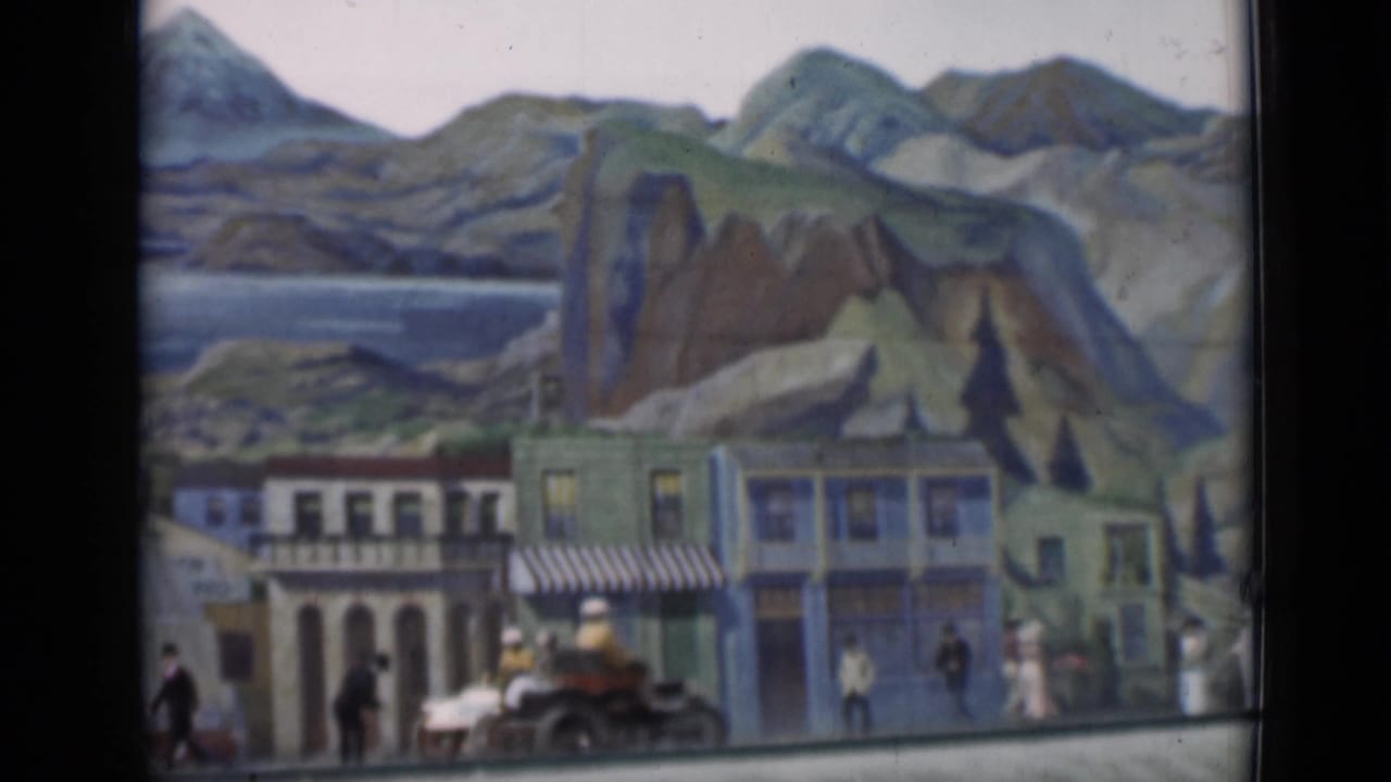1937 staged miniature street with building facades, a striped awning, tiny pedestrians, and a small vehicle below a painted mountain-and-water backdrop.