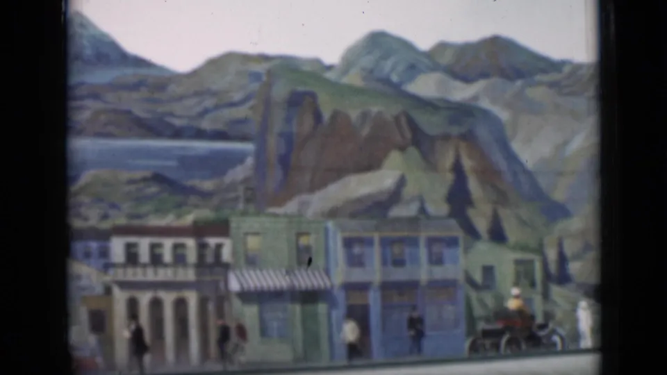 Final 1937 8mm frame of the miniature street display, showing storefront facades, tiny figures, a small vehicle, and painted mountain scenery.
