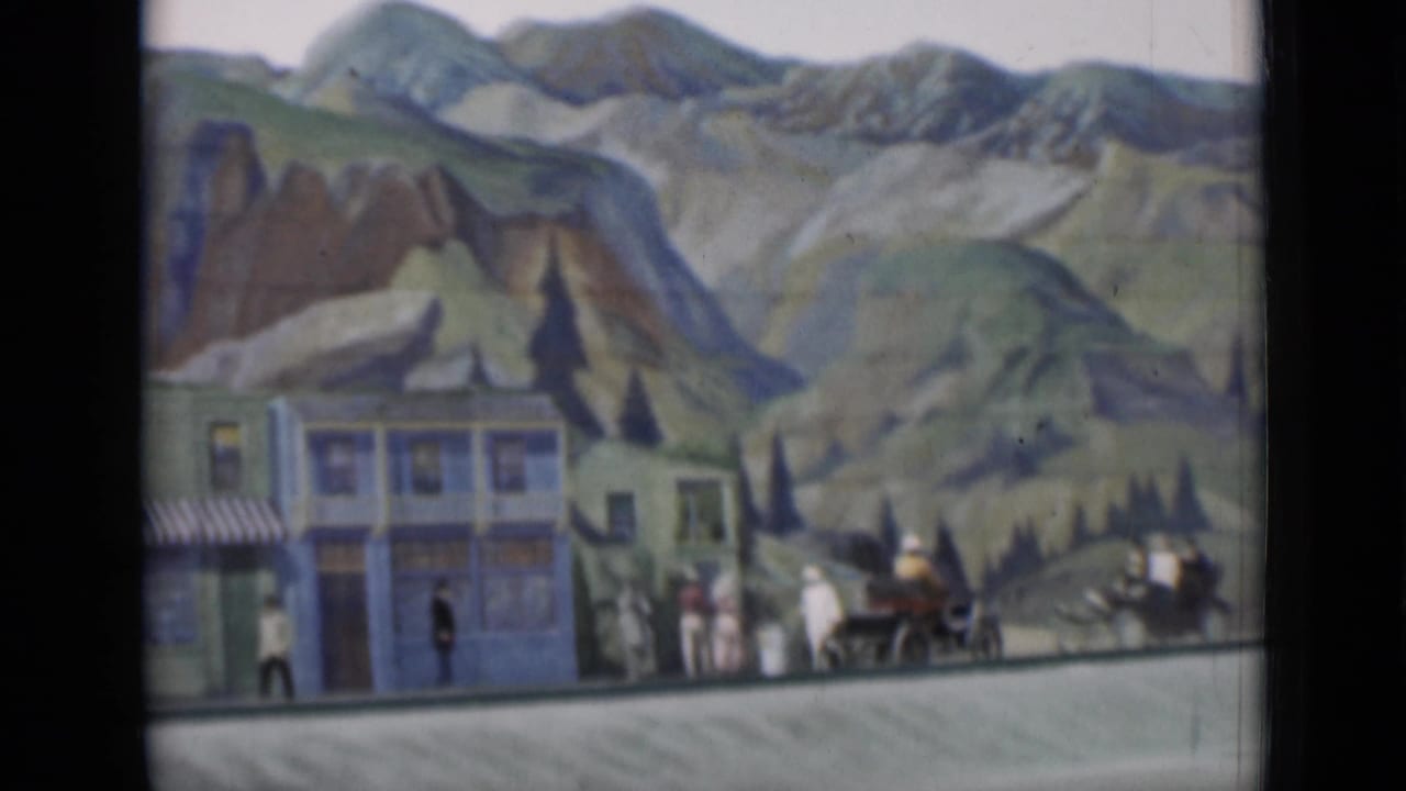 Painted mountain backdrop behind small town facades with pedestrians and a horse-drawn carriage.