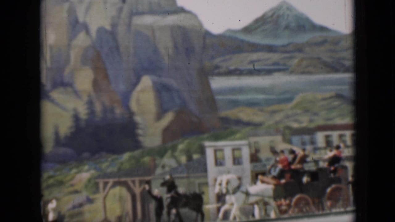 1937 San Francisco frame showing a carriage and pedestrians before a scenic painted backdrop with rock arch, water, hills, and a distant peak.