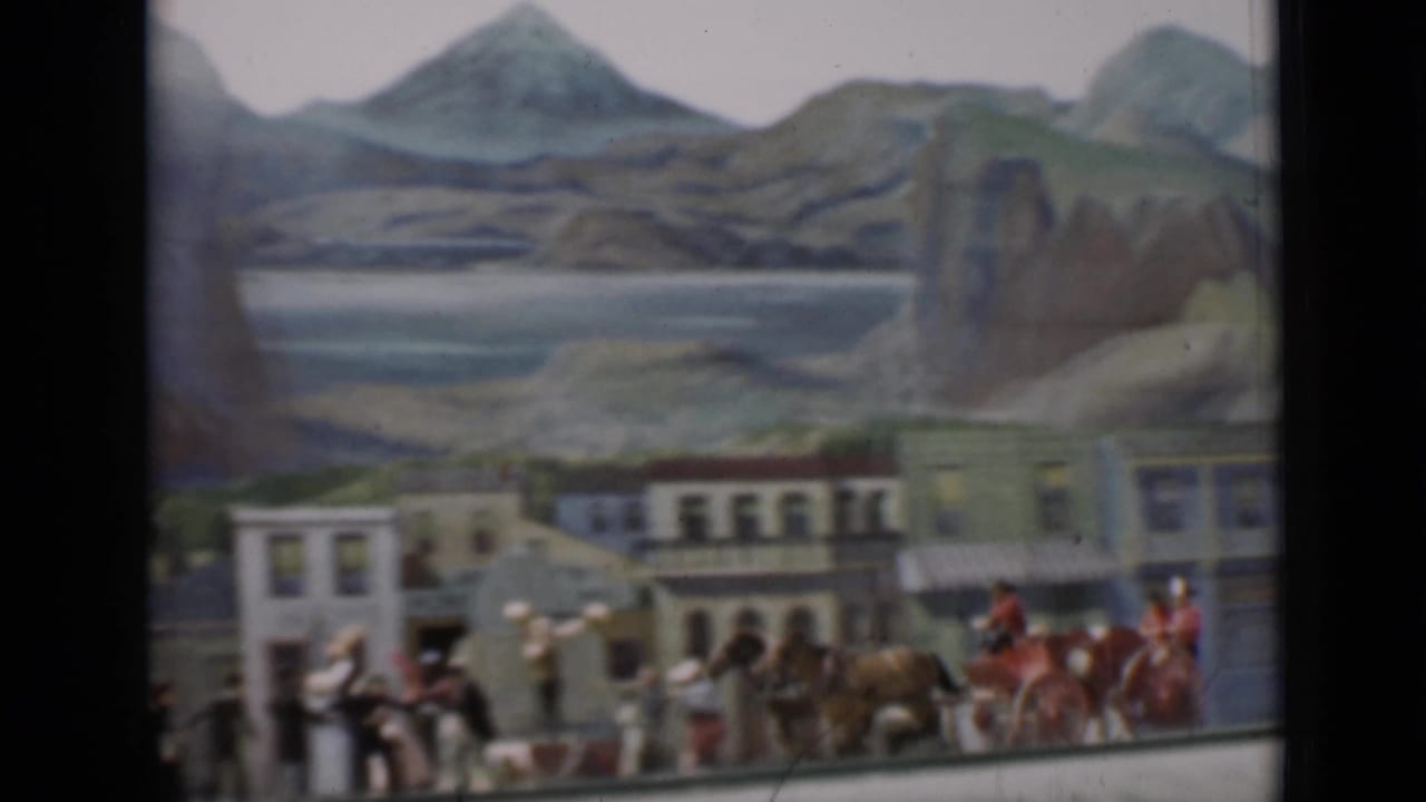 Miniature Western street with horses, figures, buildings, and painted mountains behind it.