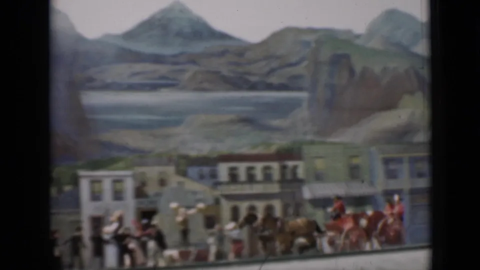 1937 San Francisco 8mm frame showing a miniature Western town street with horses, small figures, storefronts, and a painted mountain backdrop.