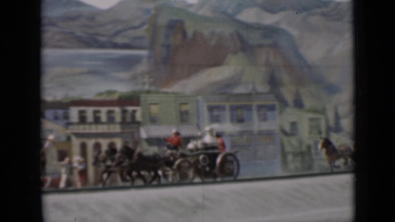 1937 San Francisco 8mm frame showing a miniature horse-drawn carriage or team near town buildings against a painted mountain scene.
