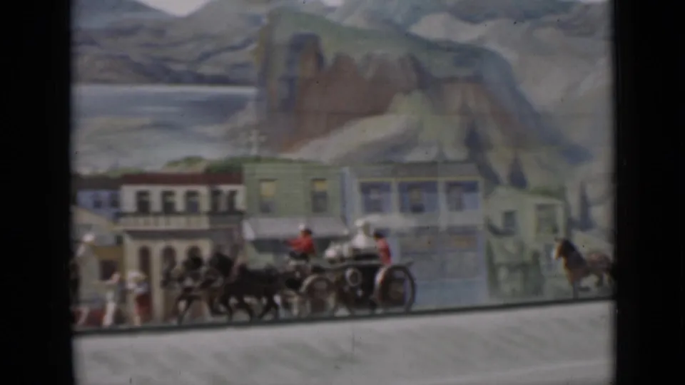 1937 San Francisco 8mm frame showing a miniature horse-drawn carriage or team near town buildings against a painted mountain scene.
