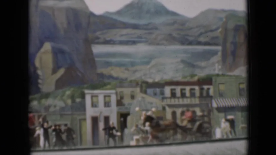 1937 San Francisco 8mm frame of a miniature Western street with a covered wagon or carriage, small figures, storefronts, and painted scenery.