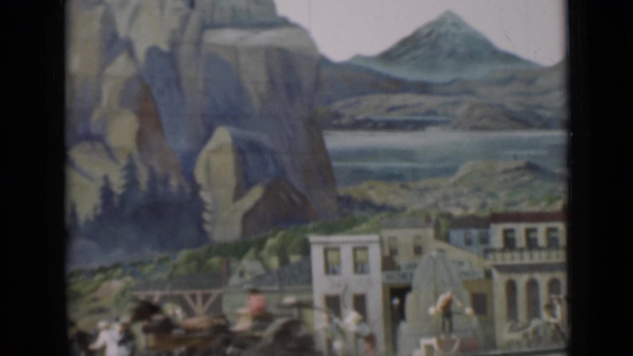 Miniature mountain town set with painted cliffs, small buildings, figures, and a carriage-like form.