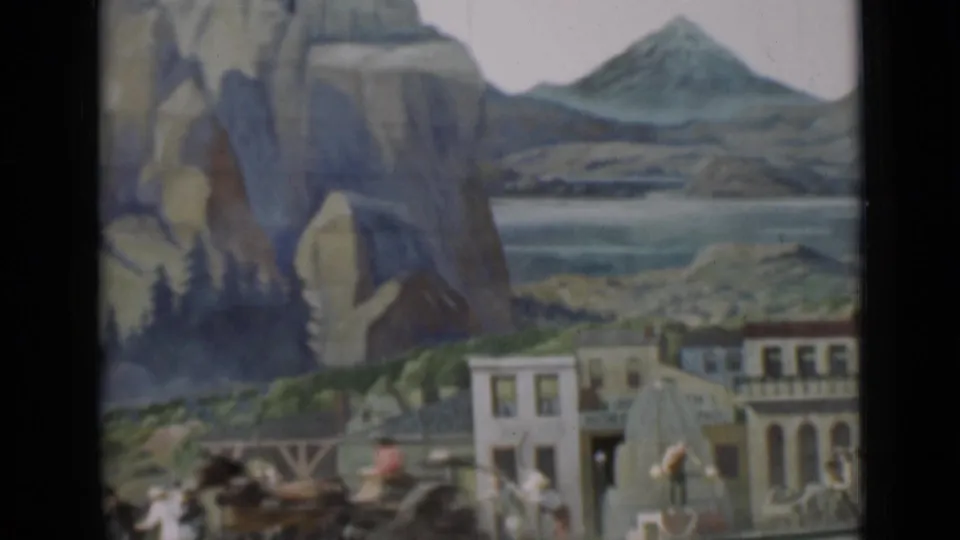 1937 San Francisco 8mm frame showing a miniature mountain-town scene with painted cliffs, small facades, tiny figures, and scenic backdrop.