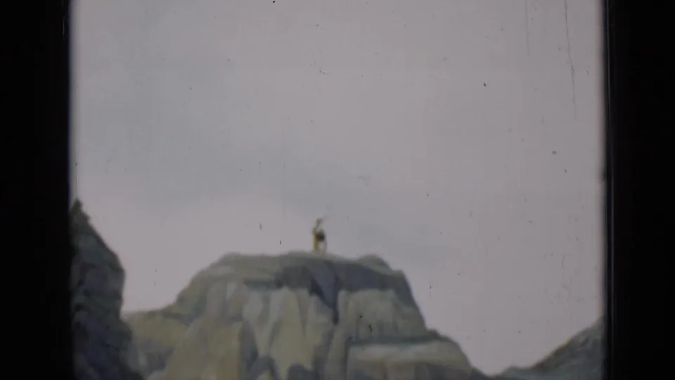 1937 San Francisco 8mm frame showing a rocky scenic model with a small figure posed on a high cliff against a pale backdrop.