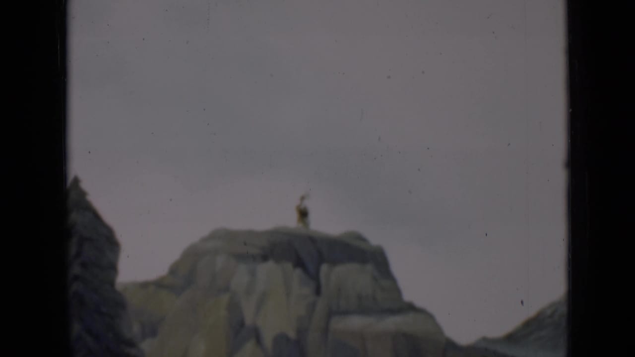 1937 San Francisco 8mm frame of a miniature rocky outcrop with a tiny standing figure and painted scenic forms near the frame edge.