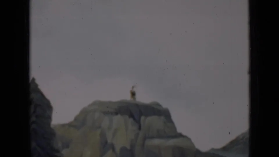 1937 San Francisco 8mm frame of a miniature rocky outcrop with a tiny standing figure and painted scenic forms near the frame edge.