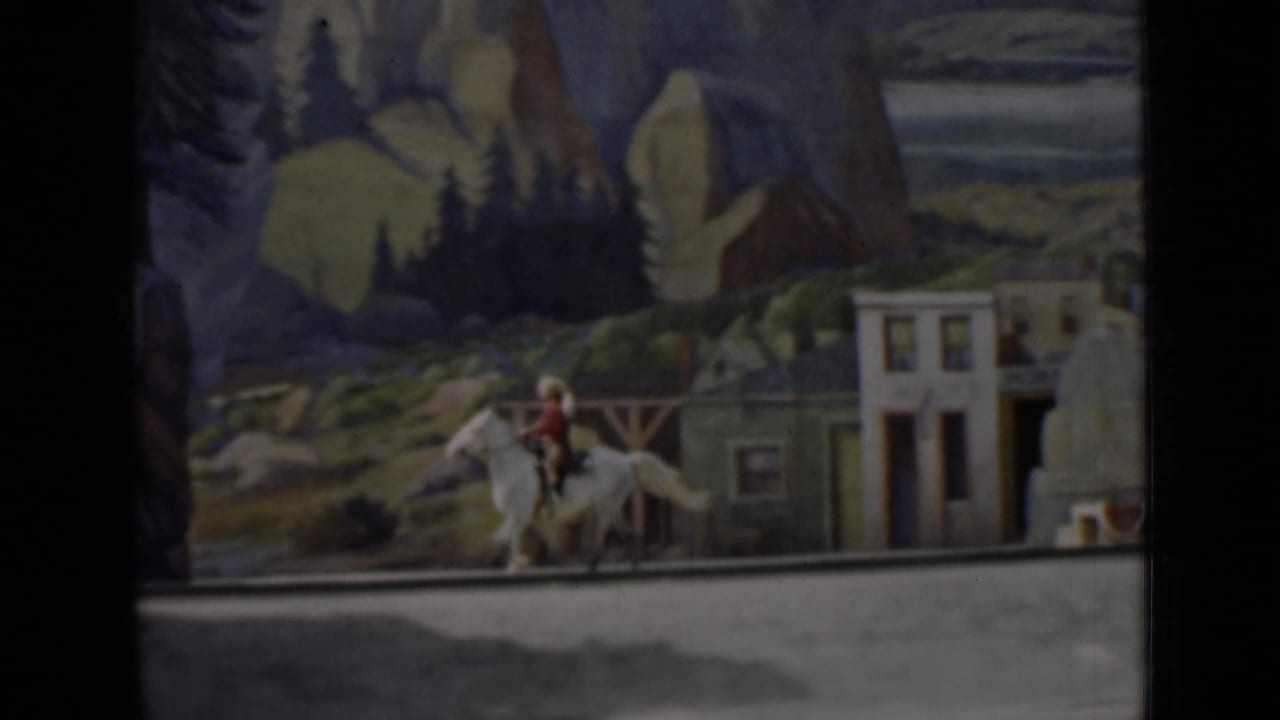 Miniature rider on a horse passes painted Western storefronts and mountain scenery.