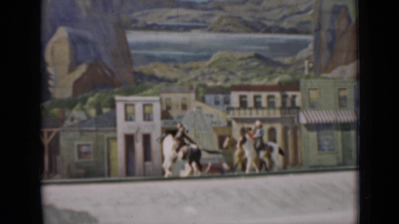 1937 San Francisco 8mm frame with miniature mounted figures near painted storefronts and scenic mountains.