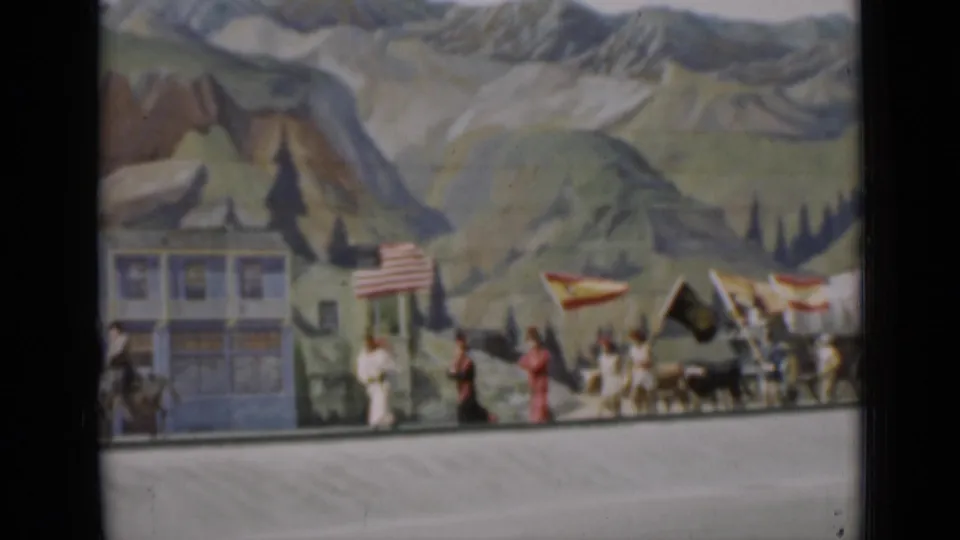 1937 San Francisco 8mm frame showing a small flag-bearing procession with figures, animals, and painted scenery.