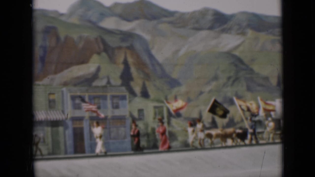 1937 San Francisco 8mm frame with a small parade, flags, figures, and a painted Western mountain backdrop.