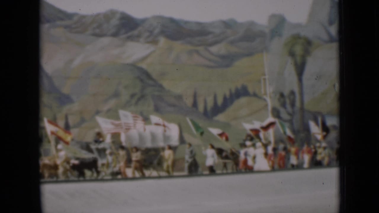 1937 San Francisco parade frame showing a wagon team, marchers, flags, and a tall painted tree in the backdrop.