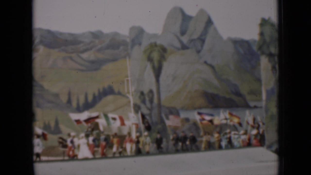 Flag bearers enter a stage before a painted mountain and palm backdrop.