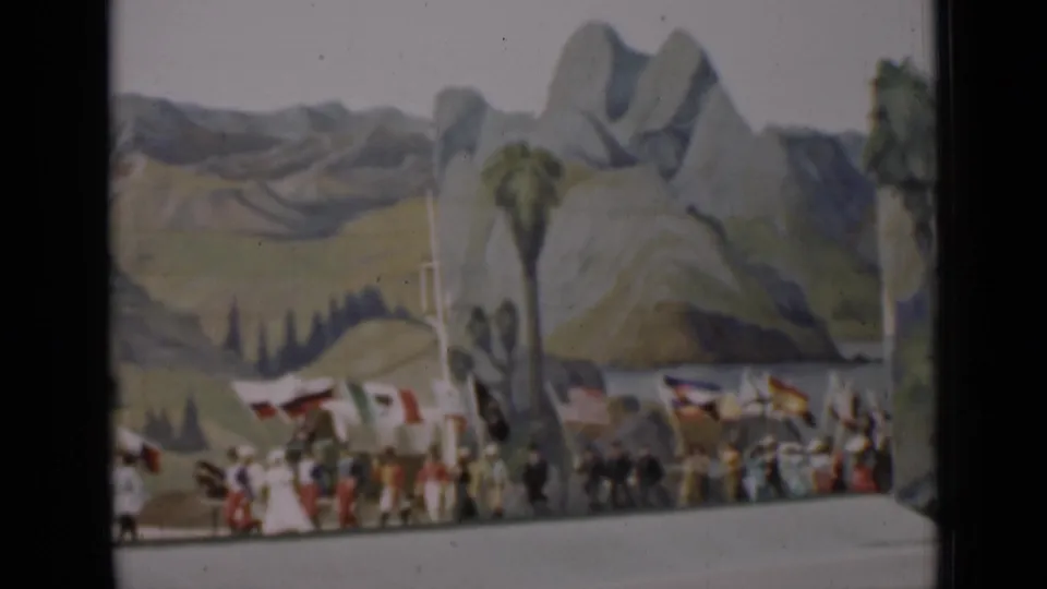 1937 San Francisco 8mm frame showing people carrying national flags across a stage with a painted landscape backdrop.