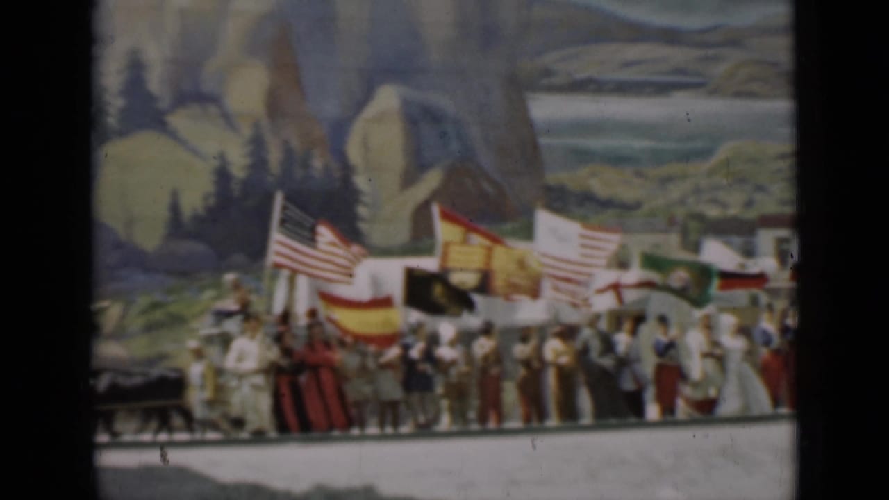 Participants gather with multiple national flags on a 1937 San Francisco stage, backed by a painted landscape scene.