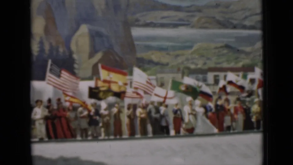 1937 San Francisco home-movie frame showing people in period dress holding American and other national flags before a painted scenic backdrop.
