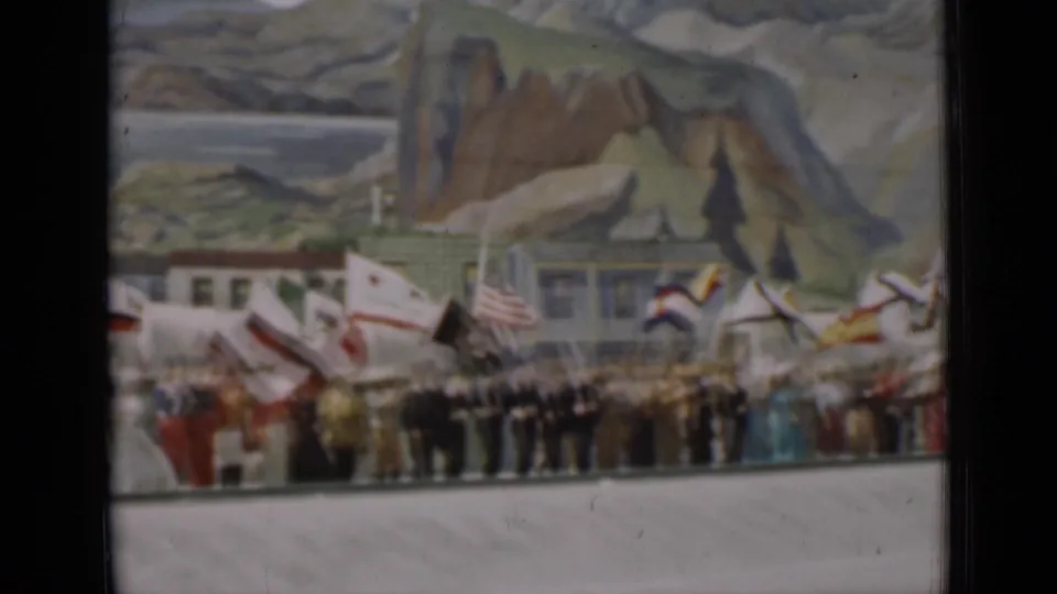 1937 San Francisco home-movie still showing a row of participants and flags beneath a large painted scenic backdrop.