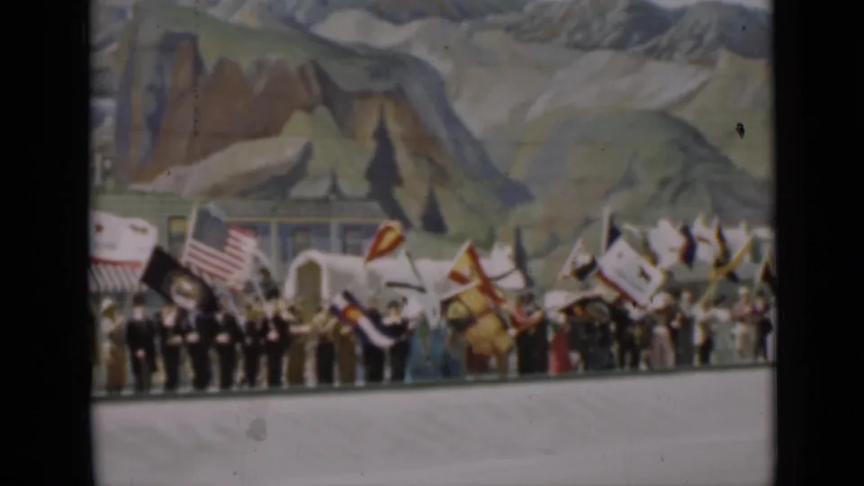 1937 San Francisco frame showing flag-bearing participants, possible uniformed men, and a painted mountain landscape backdrop at a public event.