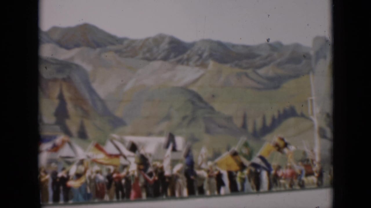 A line of people with flags stretches across a painted mountain backdrop in the 1937 San Francisco home-movie clip.