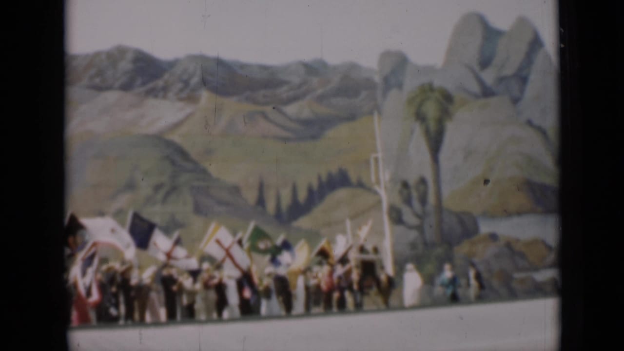 People carrying flags appear near a painted desert landscape with palm-like props and rock forms in the 1937 San Francisco footage.