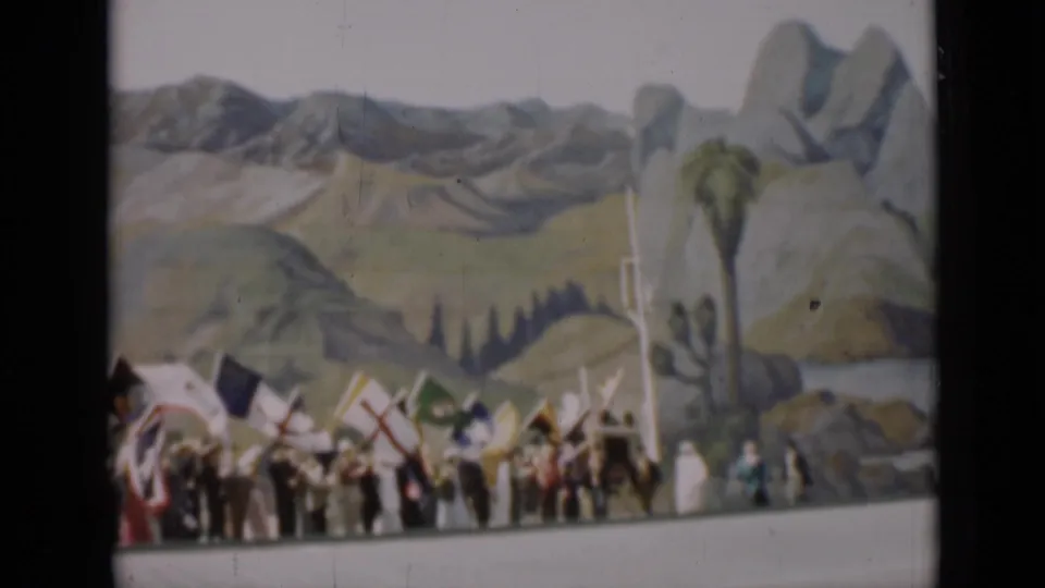 People carrying flags appear near a painted desert landscape with palm-like props and rock forms in the 1937 San Francisco footage.