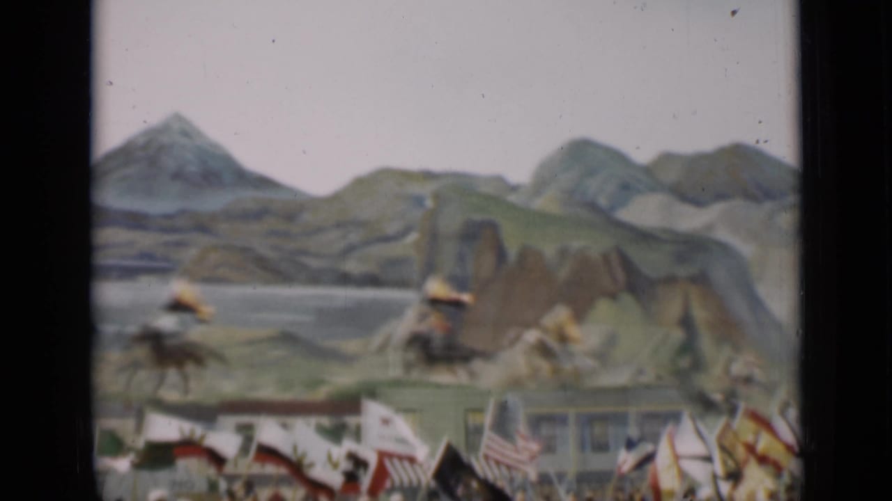 Horseback riders and flags pass before a painted mountain backdrop.
