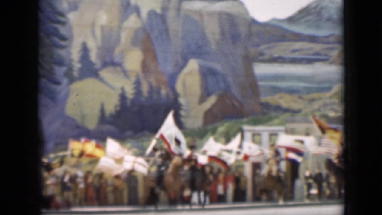 Parade participants carrying flags gather below painted cliffs and trees in the 1937 San Francisco home-movie frame.