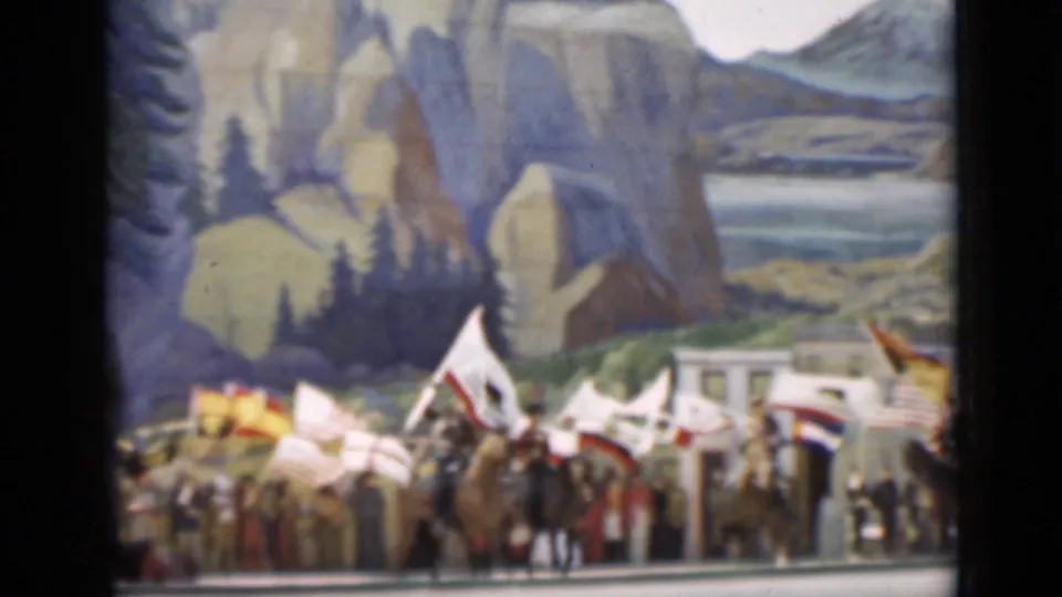 Parade participants carrying flags gather below painted cliffs and trees in the 1937 San Francisco home-movie frame.
