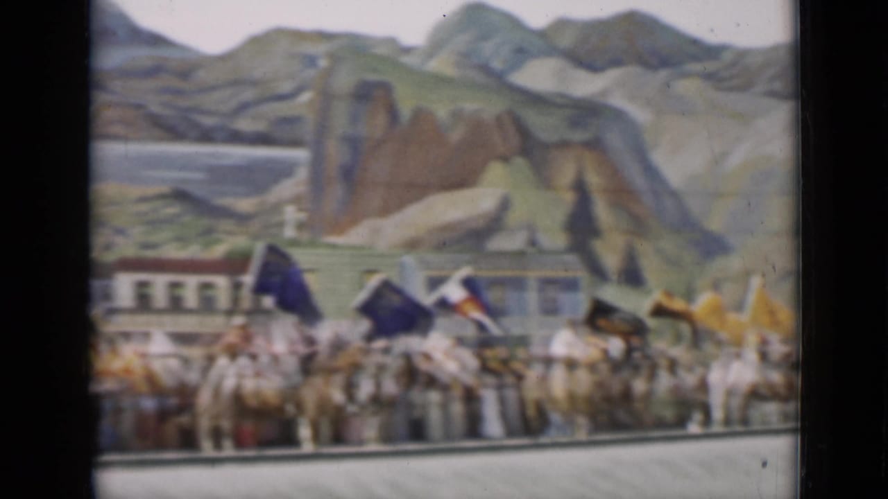 Horseback riders carrying colorful flags pass a painted mountain backdrop.