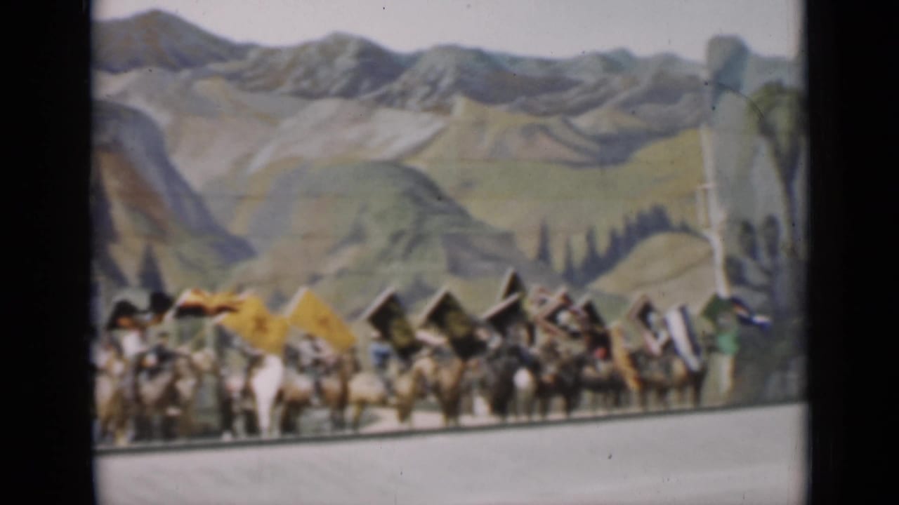 Mounted riders wave or carry flags against a painted mountain backdrop in 1937 San Francisco home-movie footage.
