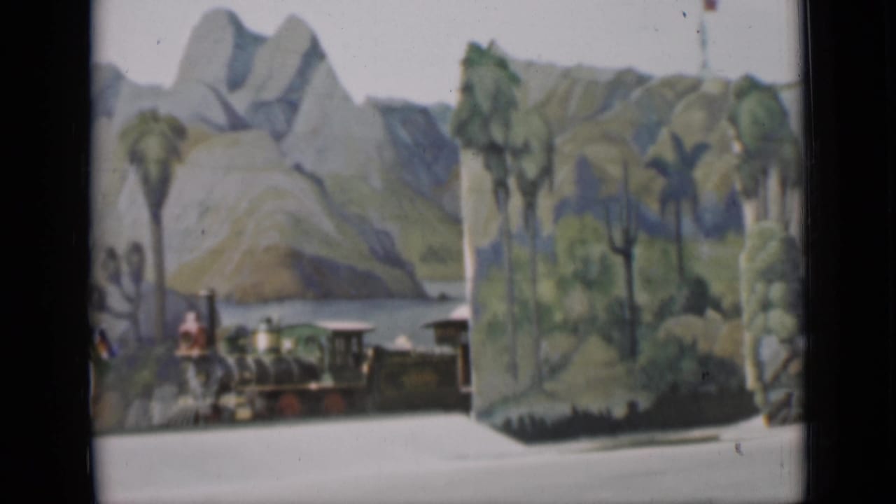 A miniature steam train in a scenic diorama with palm trees and painted hills, filmed in San Francisco in 1937.